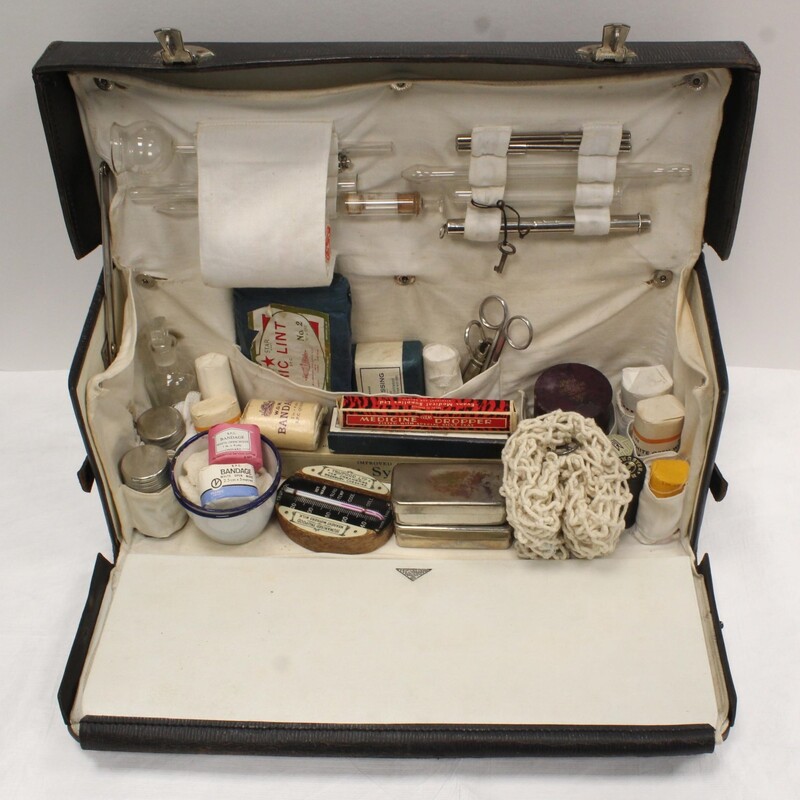 19th century, rectangular nurses case pictured open containing a variety of medical equipment including a baby-weighing net, packaged bandages in different sizes, forceps, syringes, glass tools, thermometers, and more.