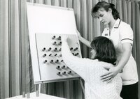 Nurse places hand on patient's back and supports her to complete a cognitive test.