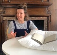 Women sits at table talking about the book laid out on the table in front of her.