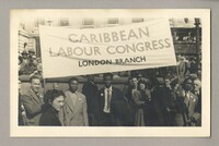 A photograph of members of the Caribbean Labour Congress (London Branch) holding up a banner with the name of their organisation. On the very left Billy Strachan can be seen holding up the banner. The rest of the people in the photograph have not been identified.