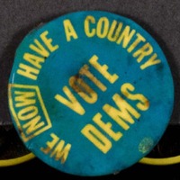 A blue badge with the slogan in yellow text 'We now have a country - vote Dems'.